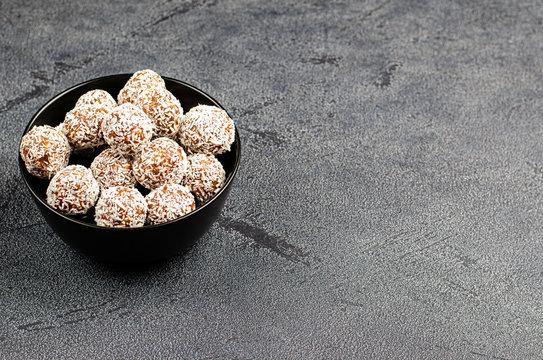 Homemade energy balls from dates, peanuts, oats, sprinkled with coconut in a black bowl on a dark background with copy space, place for text.