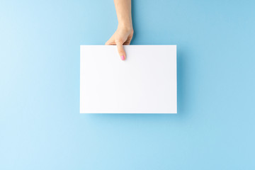 Female hand showing empty paper sheet on blue background. Close up