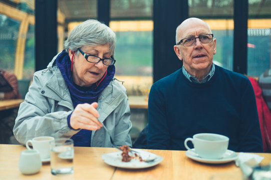 Mature couple drinking coffee and sharing cake in a cafe