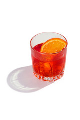 Negroni cocktail is contained in a low crystal glass with an orange slice and ice cubes. The showy illustrative picture is made on the white backdrop.