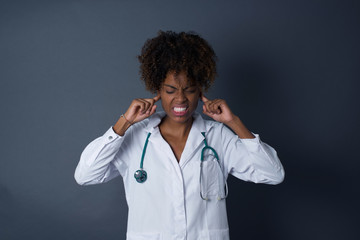 Stop making this annoying sound! Headshot of stressed out young doctor woman, plugging ears with...