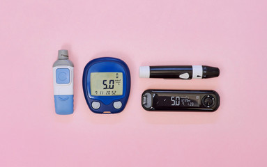 Diabetic kit: two types of glucometers, test strips, lancet. Top view, pink background, empty space.
