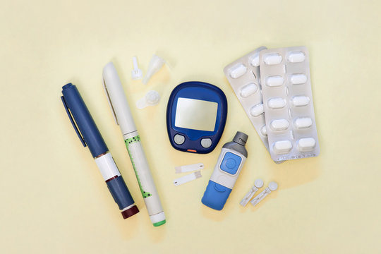 Diabetic kit: glucometer, test strips, lancet, insulin pens, metformin tablets. Top view, light yellow background.