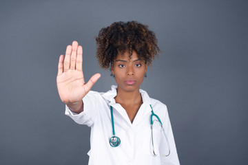 Young beautiful caucasian doctor woman doing stop gesture with palm of the hand. Warning expression with negative and serious gesture on the face isolated over gray background.