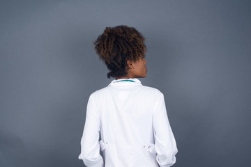 The back side view of a doctor girl with long straight wavy and shiny hair standing against gray wall. Studio Shoot.