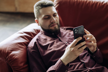  young man is lying on the couch and watching the news on his mobile phone