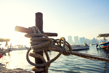 Wooden ropes wraping around rusty pole for the boat tie it on the water over city sky in Bahrain.