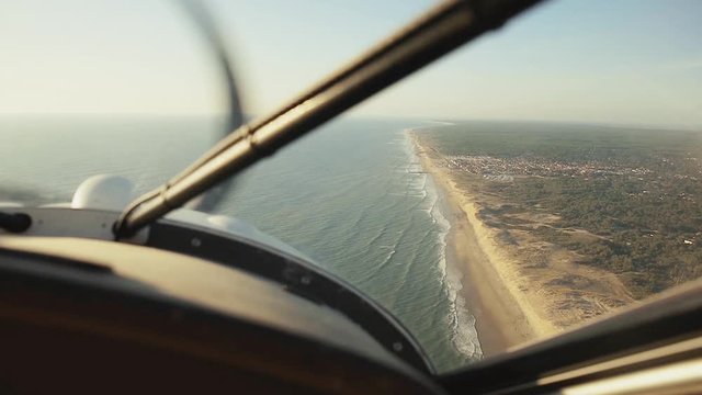 inside view from the cockpit of a flying moving plane flying over a  beach with the ocean threw the window you can see the propellers of the plane on a beautiful sunny day in montalivet France