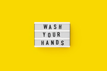 Top view flat lay on yellow background. Lightbox with wash your hands text. Covid-19 pandemic