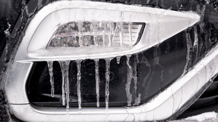 New black car in winter. Fog light close-up. Icicles and snow on the front bumper of the car. 