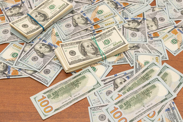 Many hundred dollar bills on wooden table background texture. bundles of money scattered on the office desk. wealth and income concept