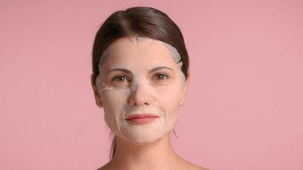 30s brunette woman portrait showing a sheet mask on touching her chinn with hand. Self-care concept