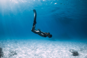 Woman freediver glides with fins over sandy sea bottom. Freediving and sun light in ocean