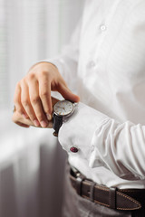 The man in the white shirt near window wears watches. Groom in wedding.