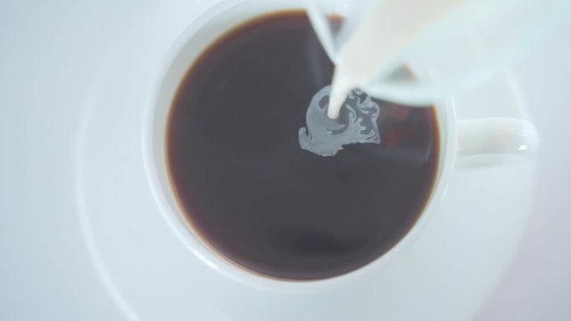 Close-up. pouring cream or milk into a coffee white cup. light background. top view