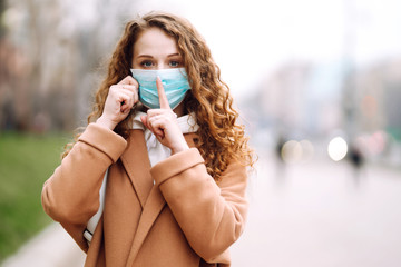 Girl in protective sterile medical mask on her face shows a gesture: shh. silence. The concept of preventing the spread of the epidemic and treating coronavirus, pandemic in quarantine city. 