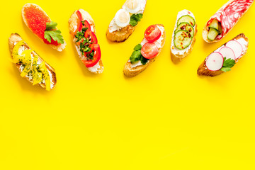 Sandwiches - set with vegetables, caviar, salami - on yellow background top-down copy space