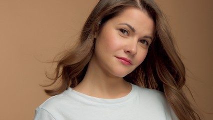 Monochrome natural makeup look Caucasian woman in studio in white t-shirtwith healthy shiny hair blowing With head slightly tilted