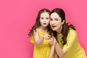 surprised mother and daughter pointing with fingers isolated on pink