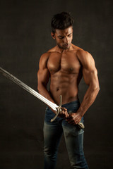 Fototapeta na wymiar Dark tanned body builder holding sword showing sculpted body