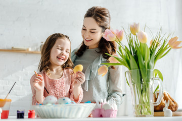selective focus of happy mother and daughter near tulips, chicken eggs and easter bread