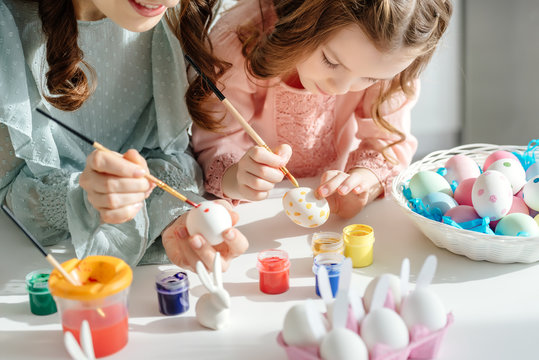 selective focus of happy mother and cute daughter painting easter eggs near decorative bunnies
