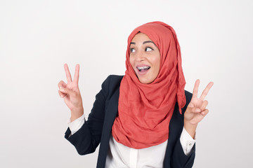 Isolated shot of cheerful European woman makes peace or victory sign with both hands, dressed in casual clothes, feels cool has toothy smile, isolated over gray background. People and body language.