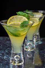 Close-up of three glasses of mojito lined up, with selective focus, with slices of lime and mint on blue marble and vertical black background