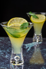 Close-up of two glasses of mojito, with selective focus, with lime and mint slices on blue marble and vertical black background