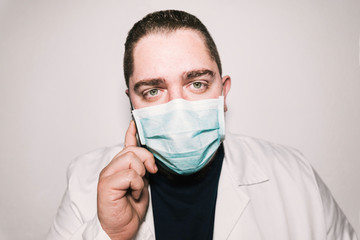 Medical stock photography wearing blue mask and white coat with green eyes .. He talks on the phone and stares.