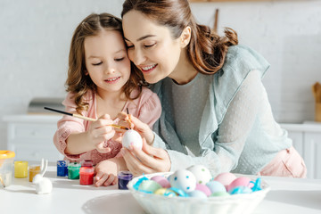 selective focus of happy mother and daughter painting chicken egg