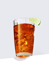 Long Island cocktail with ice cubes is contained in a highball glass with lime slice on the rim and a straw and isolated on the table edge. The showy illustrative picture is made on the gray backdrop.