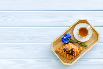 Breakfast with summer flowers. Tea, croissant and cornflowers on blue wooden background top-down copy space