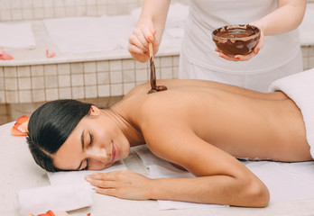 Obraz na płótnie Canvas Chocolate wrap in the spa. Young woman getting a chocolate mask on her body to moisturize her skin