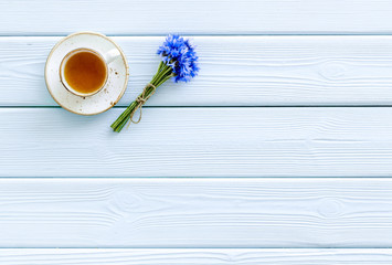 Summer tea party. Cup near cornflowers bouquet on blue wooden background top-down copy space