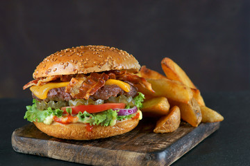 Burger with bacon, cheese and fried potatoes on a dark background
