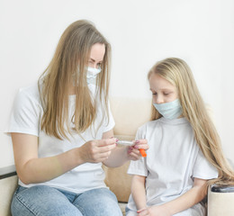 mother and daughter in medical masks learn to measure temperature on a plush toy