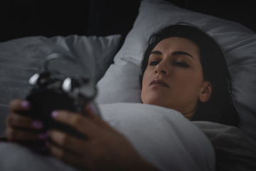 selective focus of awake woman looking at alarm clock