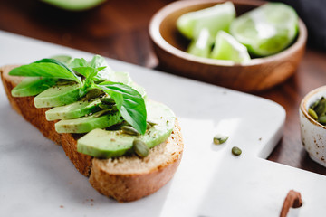 Avocado toast with pepitas and fresh basil on a white marble cutting board. Home cooking, healthy eating concept.
