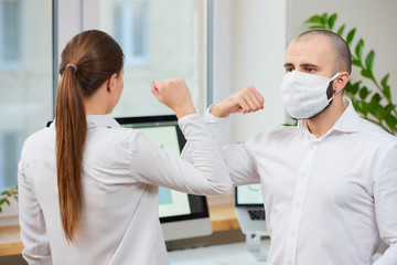 Elbow greeting to avoid the spread of coronavirus (SARS-CoV-2). Man with a medical face mask and woman meet in an office with bare hands. Instead of greeting with a hug or handshake, they bump elbows