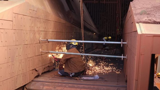 Footage of maintenance welder wearing full safety harness, helmet, mask protection uniform working on twin ropes in fall restraint position commencing hot work gouging at construction site, Perth 