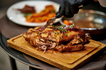 a waiter cuts a baked duck on a black board in black gloves