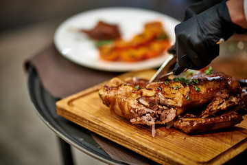 a waiter cuts a baked duck on a black board in black gloves