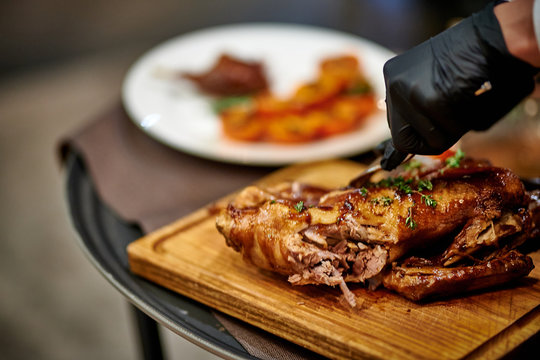 a waiter cuts a baked duck on a black board in black gloves