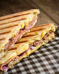 Ham and cheese sandwich on a checkered napkin, with melted cheese, ham and onion, on a toasted...
