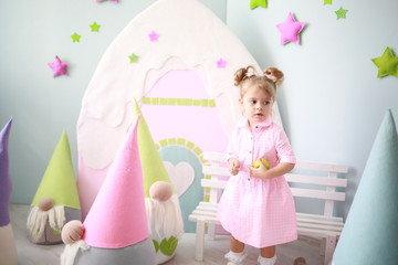 cute caucasian girl with ponytails having fun in a crowd of large toy gnomes in her bright room