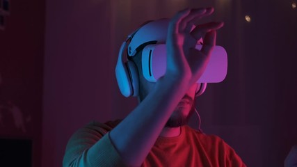 Handsome man wearing virtual reality headset. Augmented Reality. Creative man touch something using modern 3D vr glasses indoors. Freelancer student playing using VR glasses in neon lights. Shot on 4K