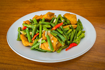 Tumis tahu kacang panjang is Indonesia food made from fresh long beans, tofu, cayenne pepper and other ingredients which is cooked by stir-frying. in white plate on wooden background