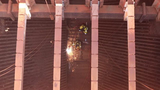 Tope view footage of rope access welder wearing full safety harness, helmet, mask protection uniform working in fall restraint commencing hot work gouging at construction mine site, Perth, Australia