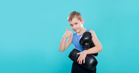 Portrait of cheerful boy with black boxing gloves on blue background